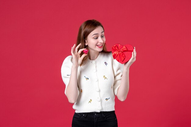 front view young female holding red heart shaped present on red background womens day shopping sensual feminine love fashion equality