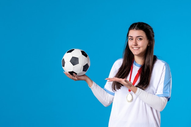 青い壁にサッカーボールを保持している若い女性の正面図