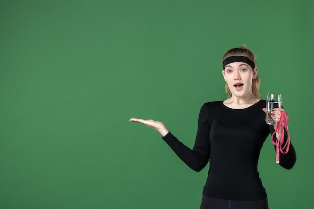 Front view young female holding waist measure and glass of water on green background color health body black workout woman athlete sport