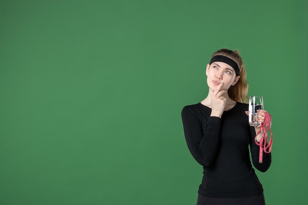 Front view young female holding waist measure and glass of water on green background color health body workout woman sport black