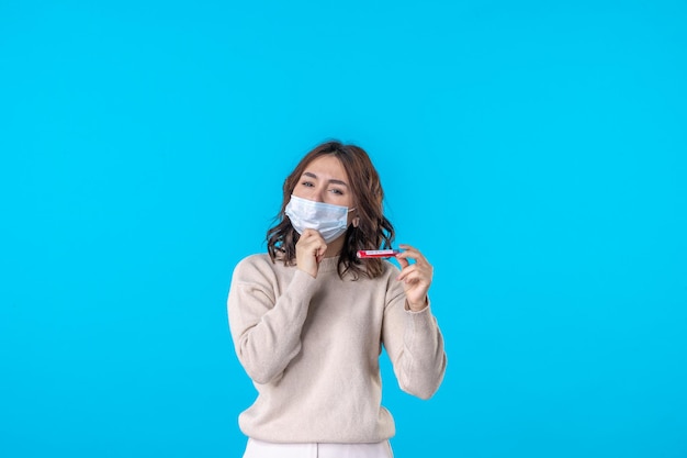 正面図青い背景の科学医療ウイルスコビッドパンデミック病の分離にフラスコとマスクで若い女性