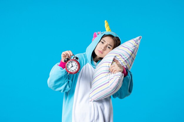 front view young female in pajama party holding pillow and clocks on blue background dream sleep late rest nightmare bed night friends fun