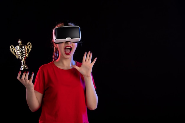 Front view of young female playing vr with winner cup on the dark wall