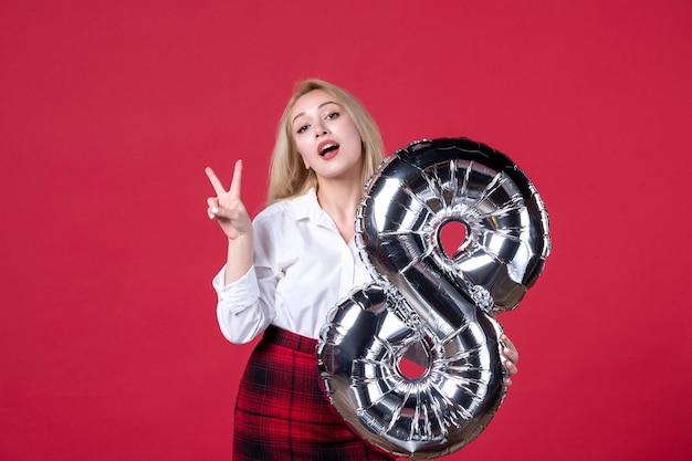 Front view young female posing with silver balloon as march symbol on red background equality sensual feminine femininity affectionate womens day colors