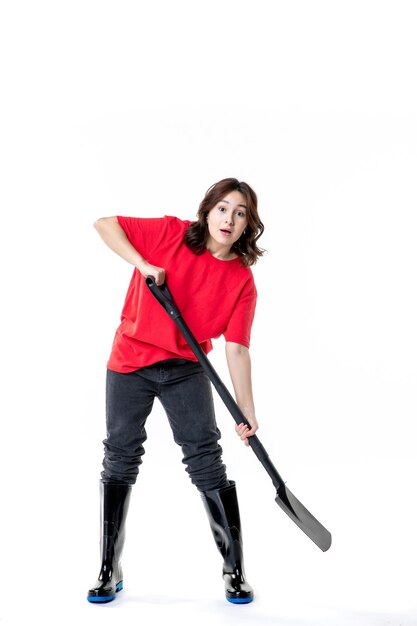 front view young female in red shirt imitating digging with black shovel on a white background soil color work woman emotion cemetery ground job