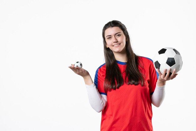 Вид спереди молодая женщина в спортивной одежде с футбольным мячом на белой стене
