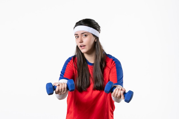 Front view young female in sport clothes working out with dumbbells on white wall