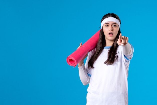 Front view young female with carpet for exercises on blue wall