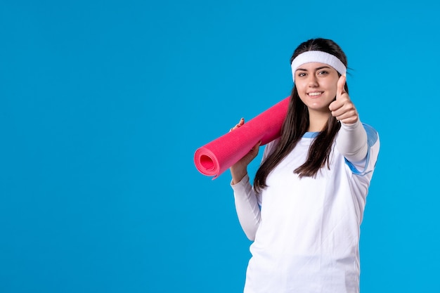 Front view young female with carpet for exercises on blue wall