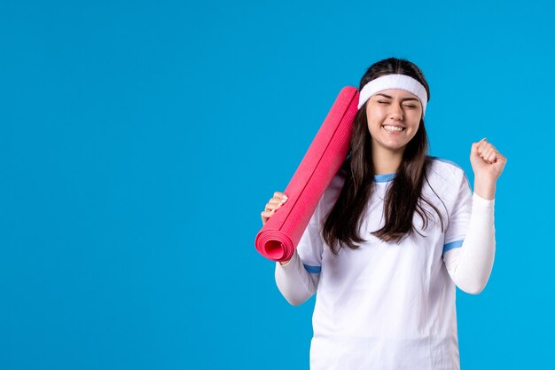 Front view young female with carpet for exercises on blue wall