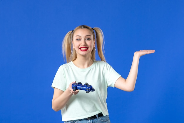 전면 보기 파란색 배경에 게임 패드가 있는 젊은 여성 즐거운 비디오 성인 플레이어 조이스틱 온라인 가상 청소년 색상 우승