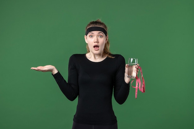 Vista frontale giovane donna con bicchiere d'acqua e misura della vita su sfondo verde salute corpo sportivo colore nero donna atleta