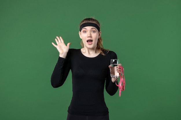 Front view young female with glass of water and waist measure on green background sport athlete woman body colors health black workout