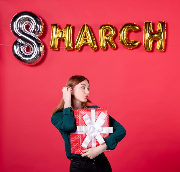 front view young female with march decoration and present on red background love vogue glamour feminine womans day gift holiday woman