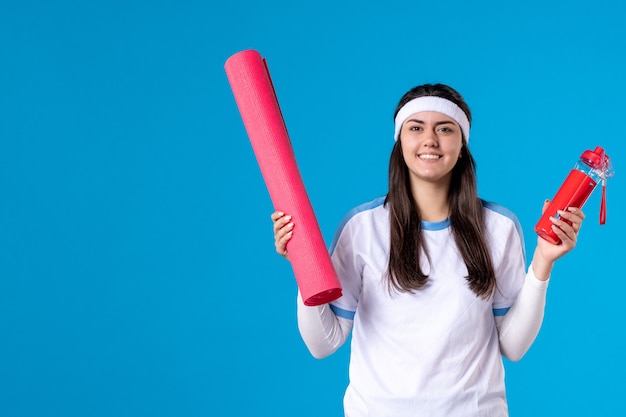 Front view young female with yoga mat on blue wall