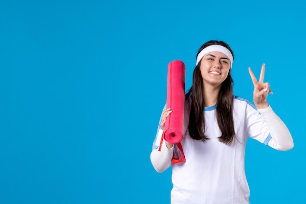 Front view young female with yoga mat on blue wall