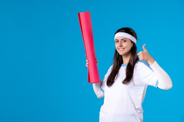 Front view young female with yoga mat on blue wall