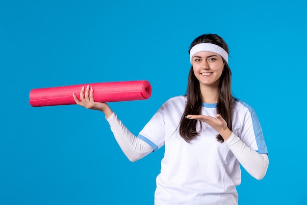 Front view young female with yoga mat on blue wall