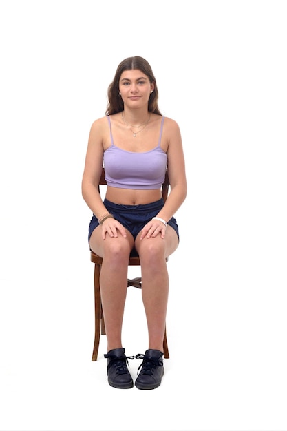 Front view of a young girl sitting on chair and looking at camera on white background