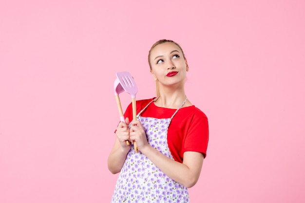 Front view young housewife holding cutlery on pink wall