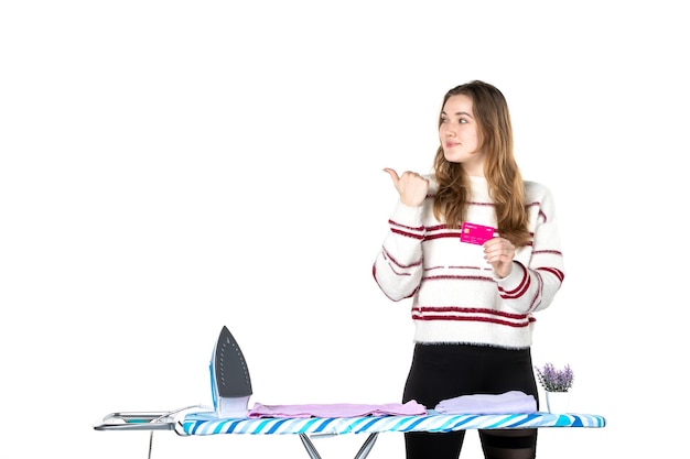 Front view young housewife holding pink bank card on white background housework laundry cleaning clothes woman money