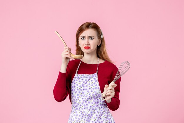 Front view young housewife holding whisk and wooden spoon on pink background cake cuisine profession horizontal uniform dough woman pie