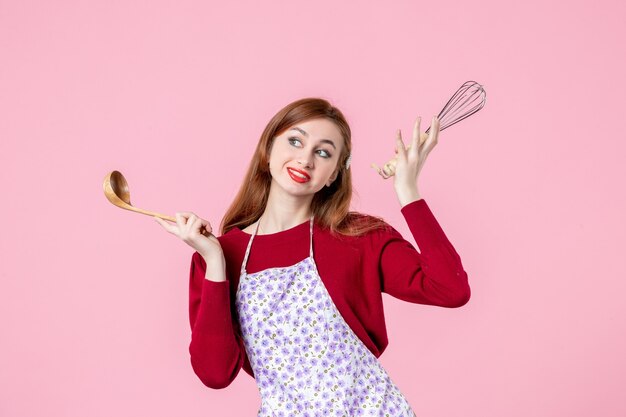 front view young housewife holding whisk and wooden spoon on pink background cooking cuisine cake uniform pie profession dough woman