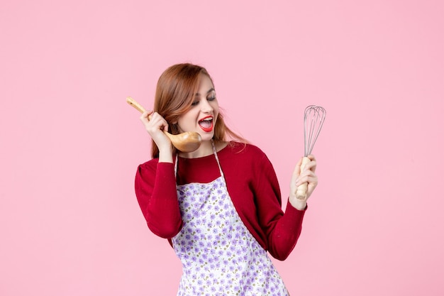 front view young housewife holding whisk and wooden spoon on pink background horizontal pie woman cooking uniform profession cake dough