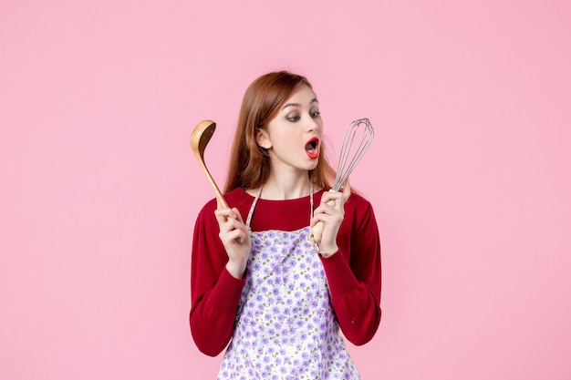 front view young housewife holding whisk and wooden spoon on pink background woman dough cake cuisine horizontal uniform pie profession