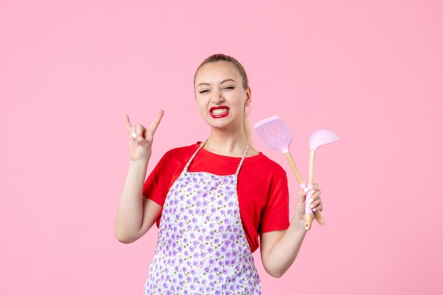 Front view young housewife posing with cutlery in her hands on pink wall