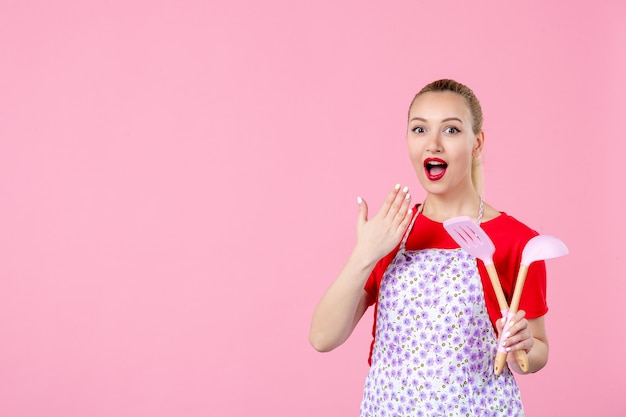 Front view young housewife posing with cutlery on pink wall