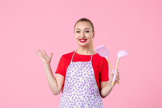 Front view young housewife posing with cutlery on pink wall