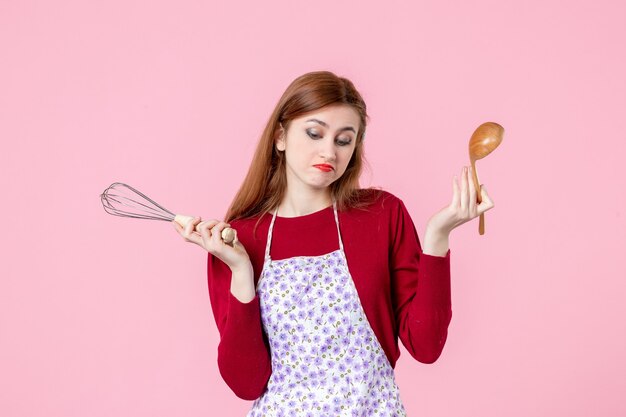 front view young housewife posing with whisk and wooden spoon on pink background cake profession cooking dough uniform pie cuisine woman