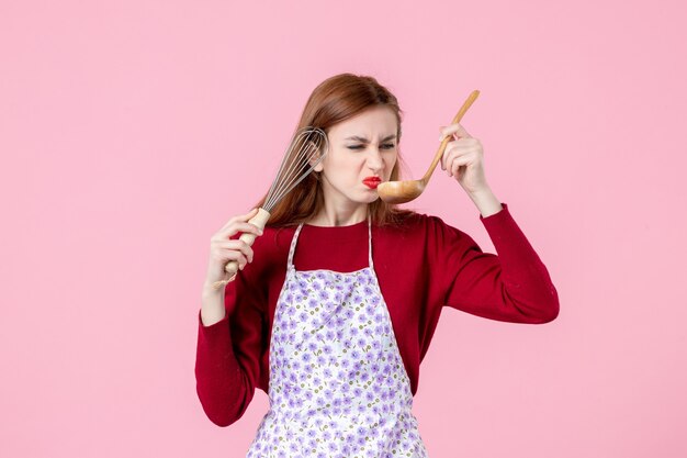 front view young housewife posing with whisk and wooden spoon on pink background cake profession dough woman uniform horizontal pie cuisine