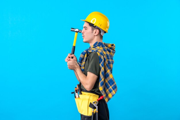 front view young male builder holding hammer on the blue background worker house job building architecture constructor flat