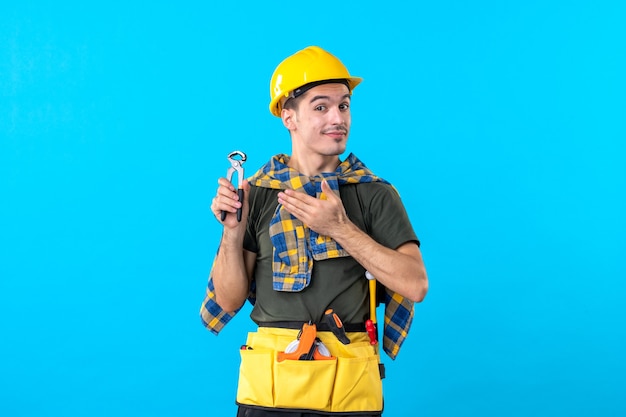 front view young male builder with different tools on the blue background building flat job worker constructor architecture house