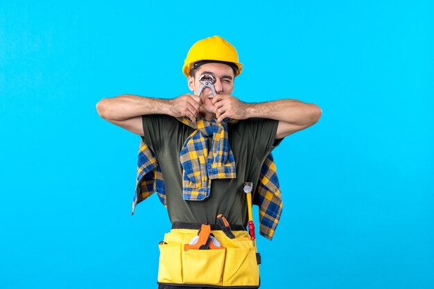 Front view young male builder with different tools on a blue background job worker house constructor building flat architecture