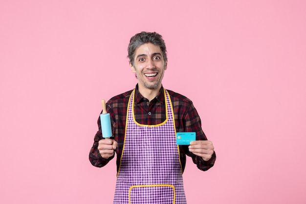 正面図ピンクの背景に小さな麺棒と銀行カードを保持している岬の若い男性お金の職業夫料理仕事労働者キッチン制服
