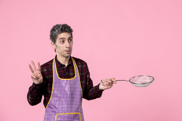 front view young male in cape holding sieve on pink background cook job profession husband kitchen horizontal food worker color