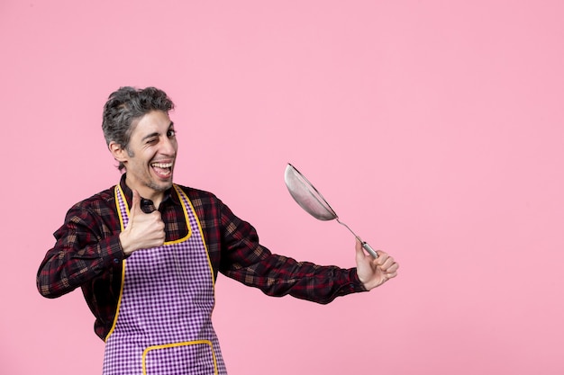 front view young male in cape holding sieve and preparing to hit something on pink background profession color cook husband worker horizontal food kitchen job uniform