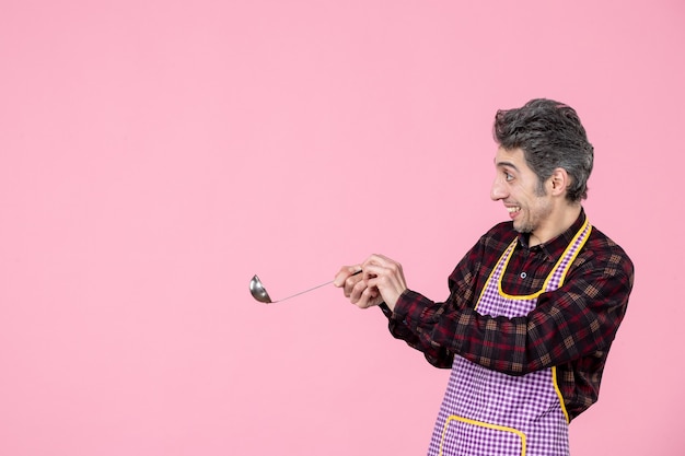 front view young male in cape holding silver soup spoon on pink background cook cuisine worker kitchen food horizontal profession