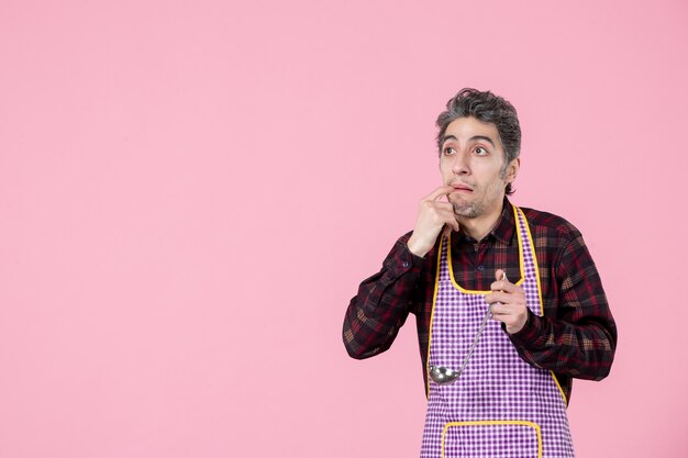 front view young male in cape holding soup spoon and looking at something pink background job profession horizontal cook worker food husband