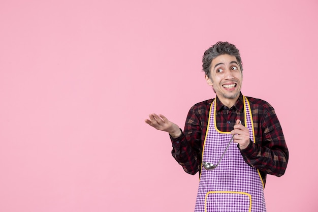 front view young male in cape holding soup spoon and looking at something pink background job profession horizontal cook worker husband kitchen