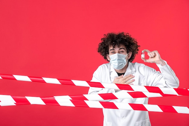 Foto vista frontale giovane medico maschio in uniforme medica che tiene il pallone sullo sfondo rosso pericolo ospedale quarantena covid-striscia colore avvertenza salute