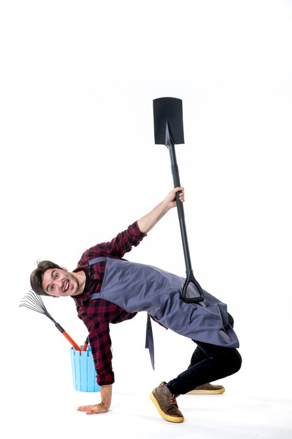 front view young male gardener holding black shovel on white background uniform soil work job green ground flower garden tree digging