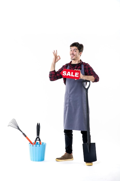 front view young male gardener with black shovel and sale writing on white background garden digging uniform work ground soil flower