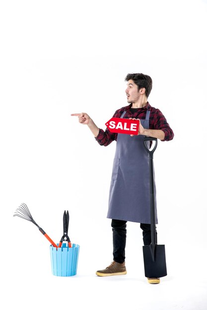 front view young male gardener with black shovel and sale writing on the white background garden digging uniform work job ground soil flower