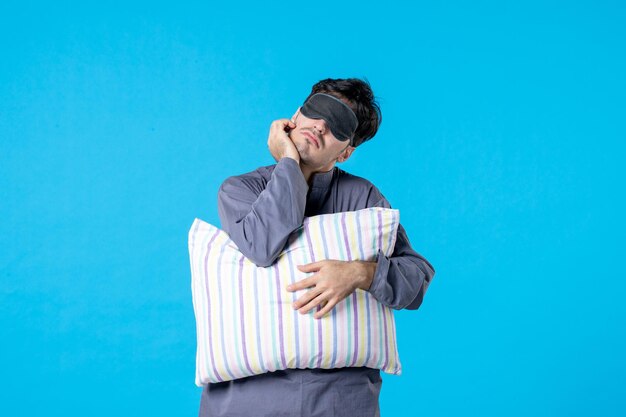 front view young male in his pajamas and bandage for sleep holding pillow on blue background color late nightmare human rest wake sleep dream bed