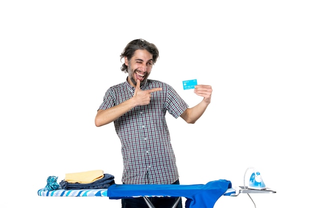 front view young male holding bank card behind ironing board on white background iron machine home money housework man dry laundry