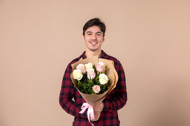 Front view young male holding beautiful flowers on brown wall